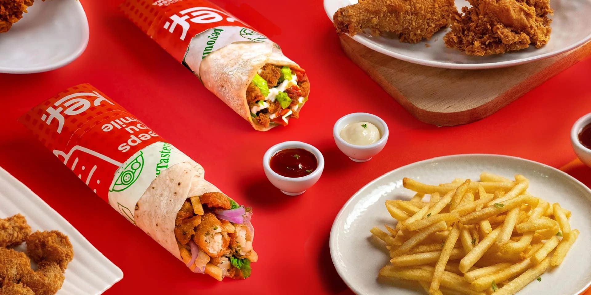 A KEF spread of wraps, fried chicken and fries on red studio paper